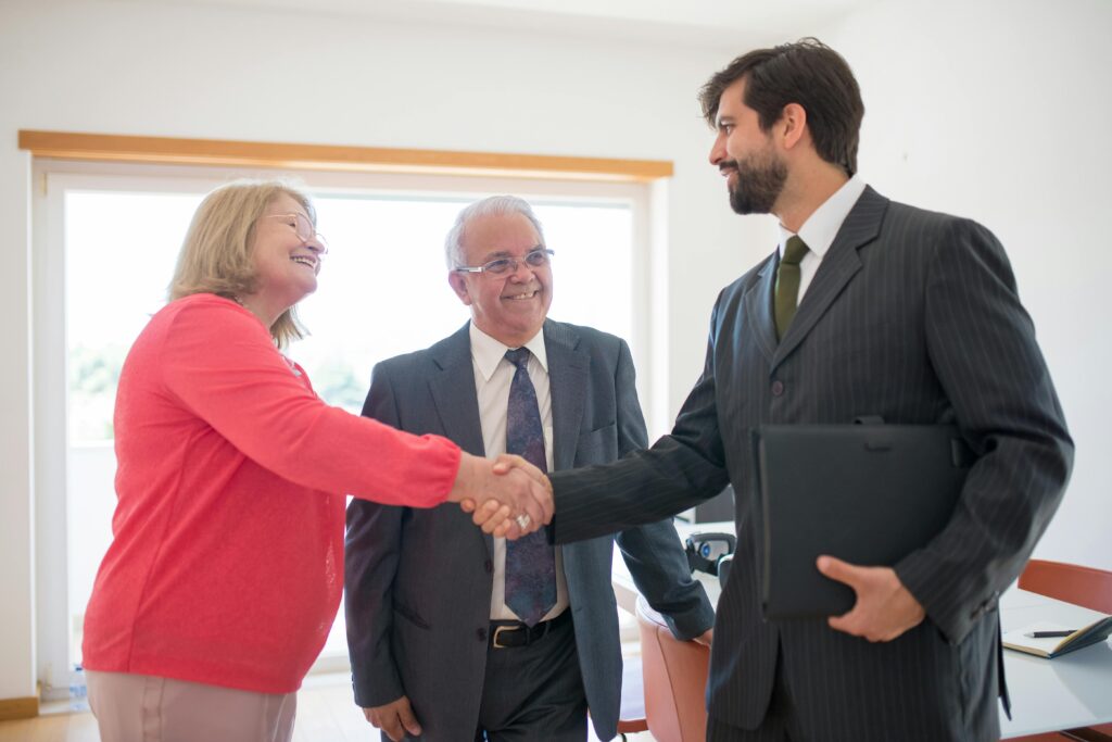 Senior couple meeting with a real estate agent indoors, shaking hands to finalize a home agreement.